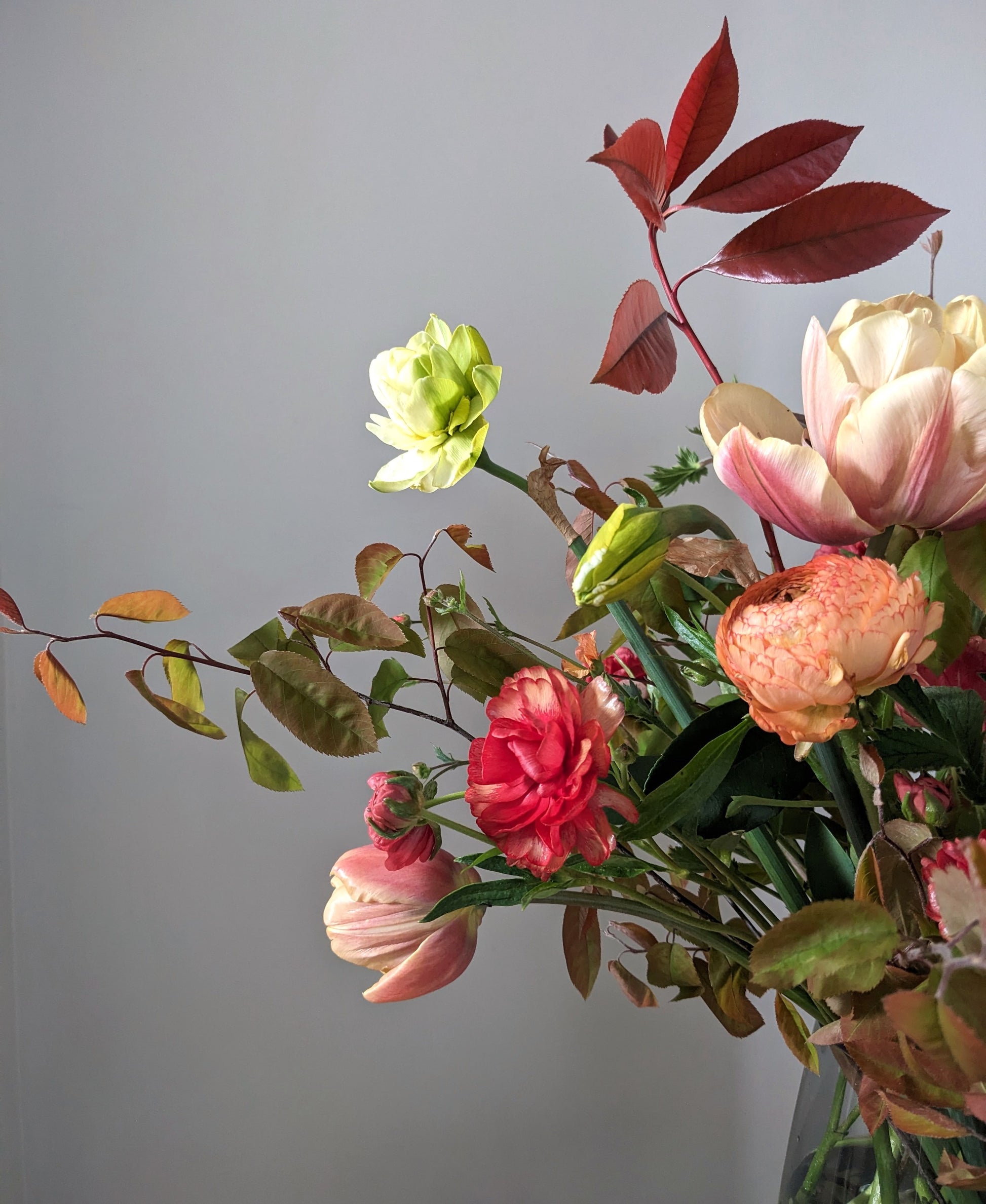 Vase arrangement of British grown flowers and foliage in peach, orange and red